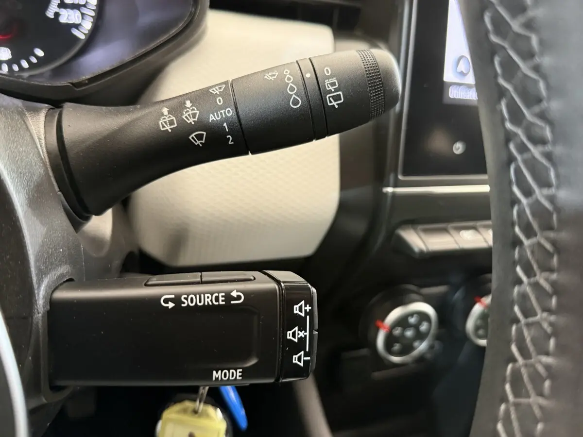 Gros plan sur les commandes au volant d’une Renault Clio blanche, avec levier d’essuie-glace et bouton source mode.