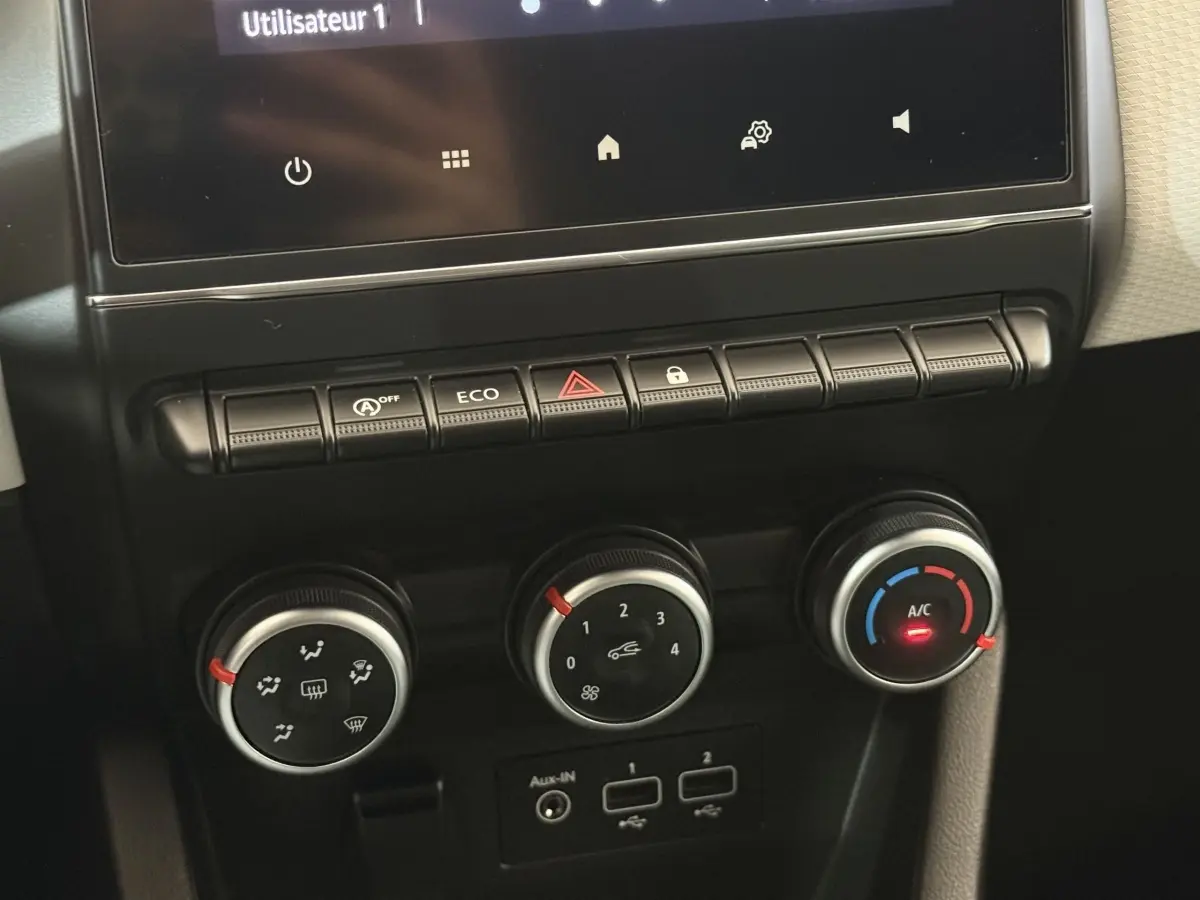 Gros plan sur la console centrale de la Renault Clio blanche 2023, montrant les commandes de climatisation et boutons multifonctions.