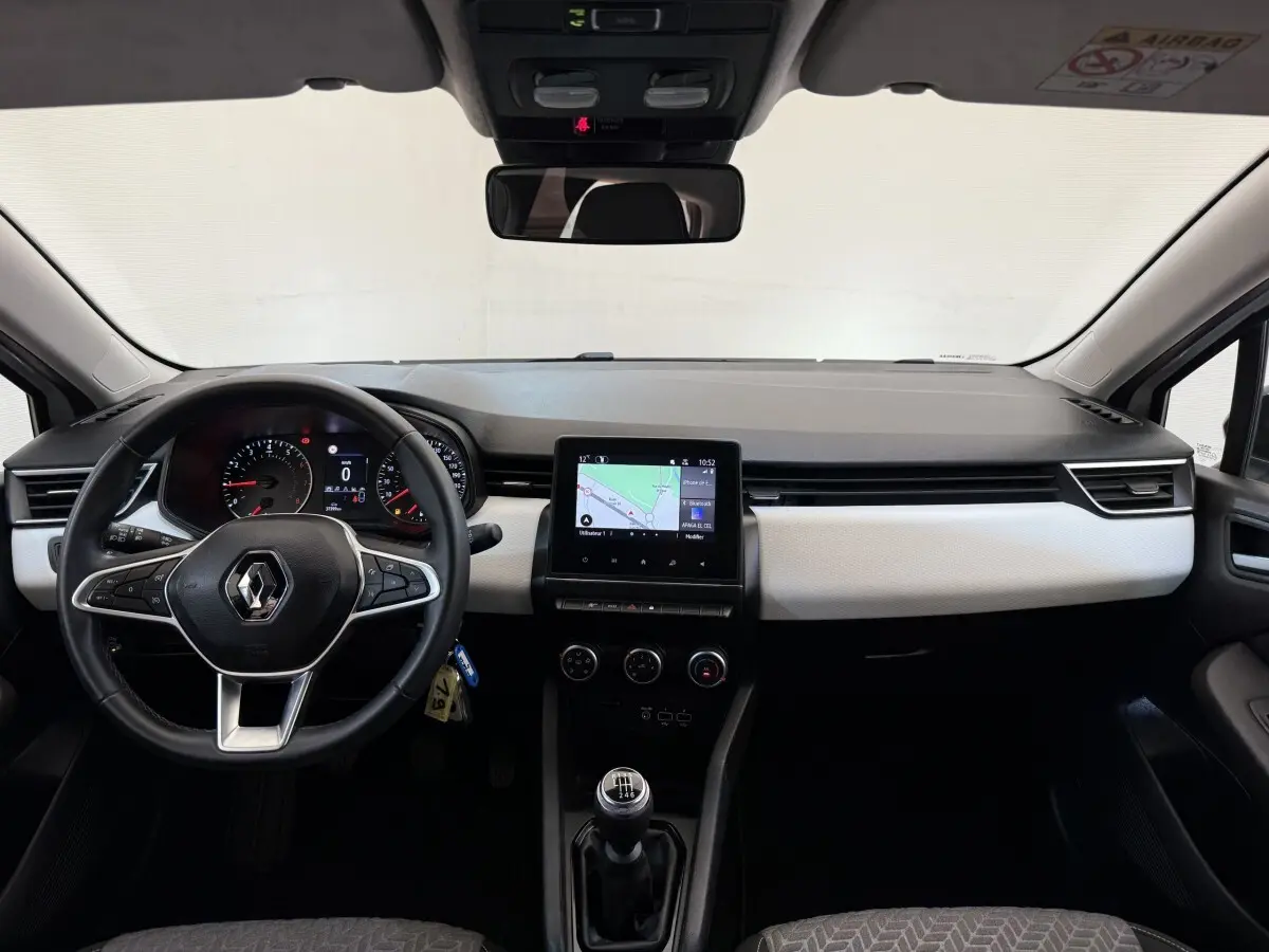 Vue intérieure avant de la Renault Clio Evolution TCe 100 GPL 2023, tableau de bord noir et blanc avec écran tactile central et volant cuir noir.