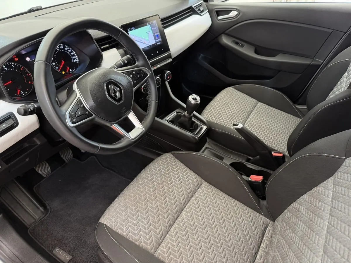 Intérieur de Renault Clio 2023 vu côté conducteur, volant cuir, sièges gris à motifs, écran tactile central avec navigation.
