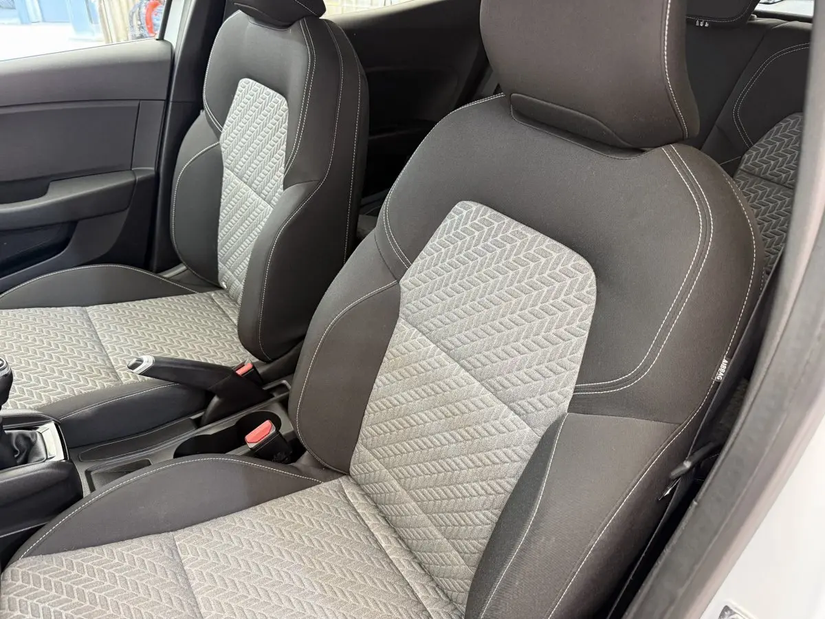 Vue intérieure des sièges avant gris et noirs de la Renault Clio Evolution TCe 100 GPL 2023, avec volant et levier de vitesses visibles.