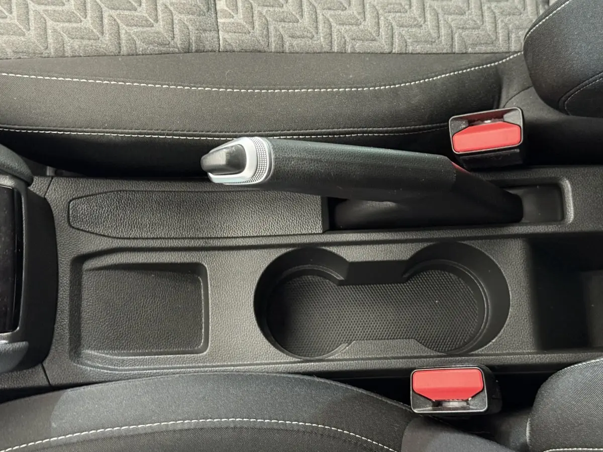Vue plongeante sur le frein à main noir et les porte-gobelets entre les sièges avant noirs de la Renault Clio Evolution TCe 100 GPL.