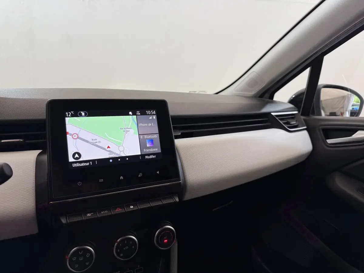 Vue intérieure côté passager de la Renault Clio blanche 2023, avec écran tactile de navigation affiché au centre du tableau de bord.