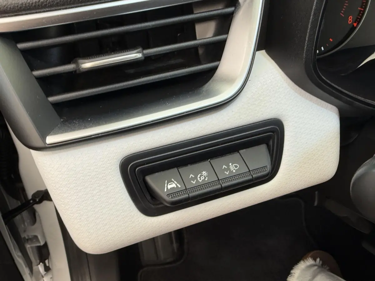 Gros plan sur les commandes d'assistance et réglages d'éclairage intégrées au tableau de bord blanc côté gauche de la Renault Clio.