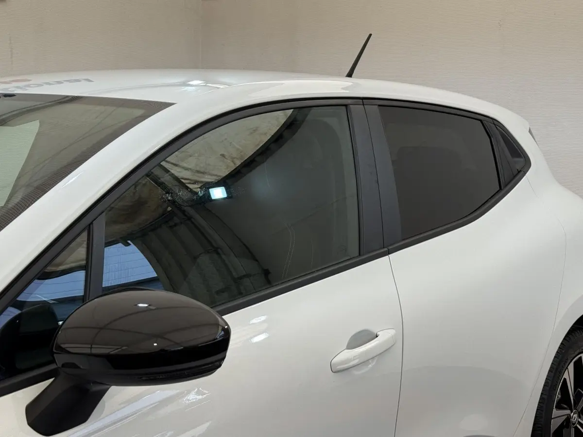 Vue latérale gauche d'une Renault Clio Evolution TCe 100 GPL blanche avec rétroviseur noir brillant et vitres teintées.