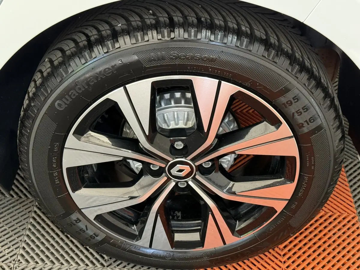 Gros plan sur la jante alliage bicolore noire et argent avec logo Renault, montée sur pneu 195/55 R16 d'une Clio blanche.