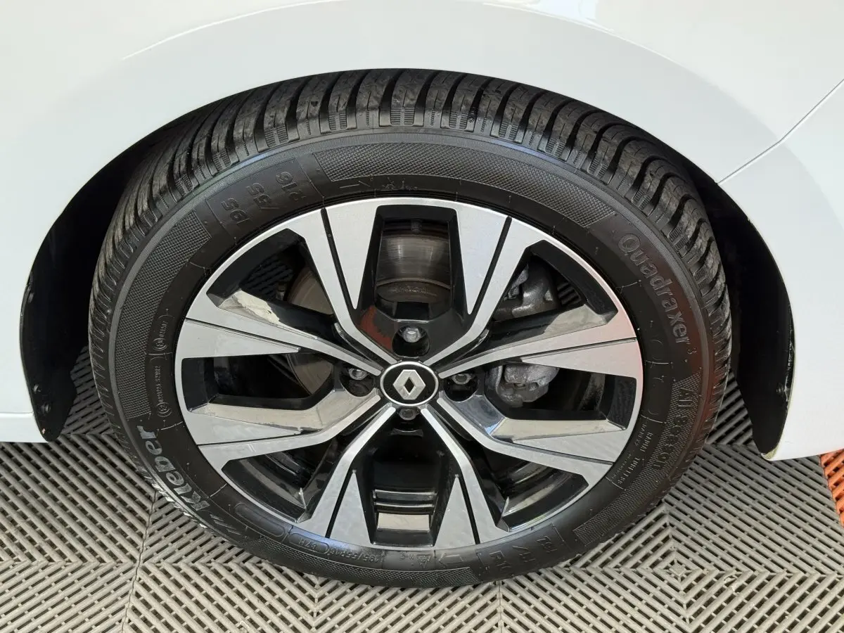 Gros plan sur la roue avant droite d’une Renault Clio blanche, mettant en valeur la jante alliage au design moderne.