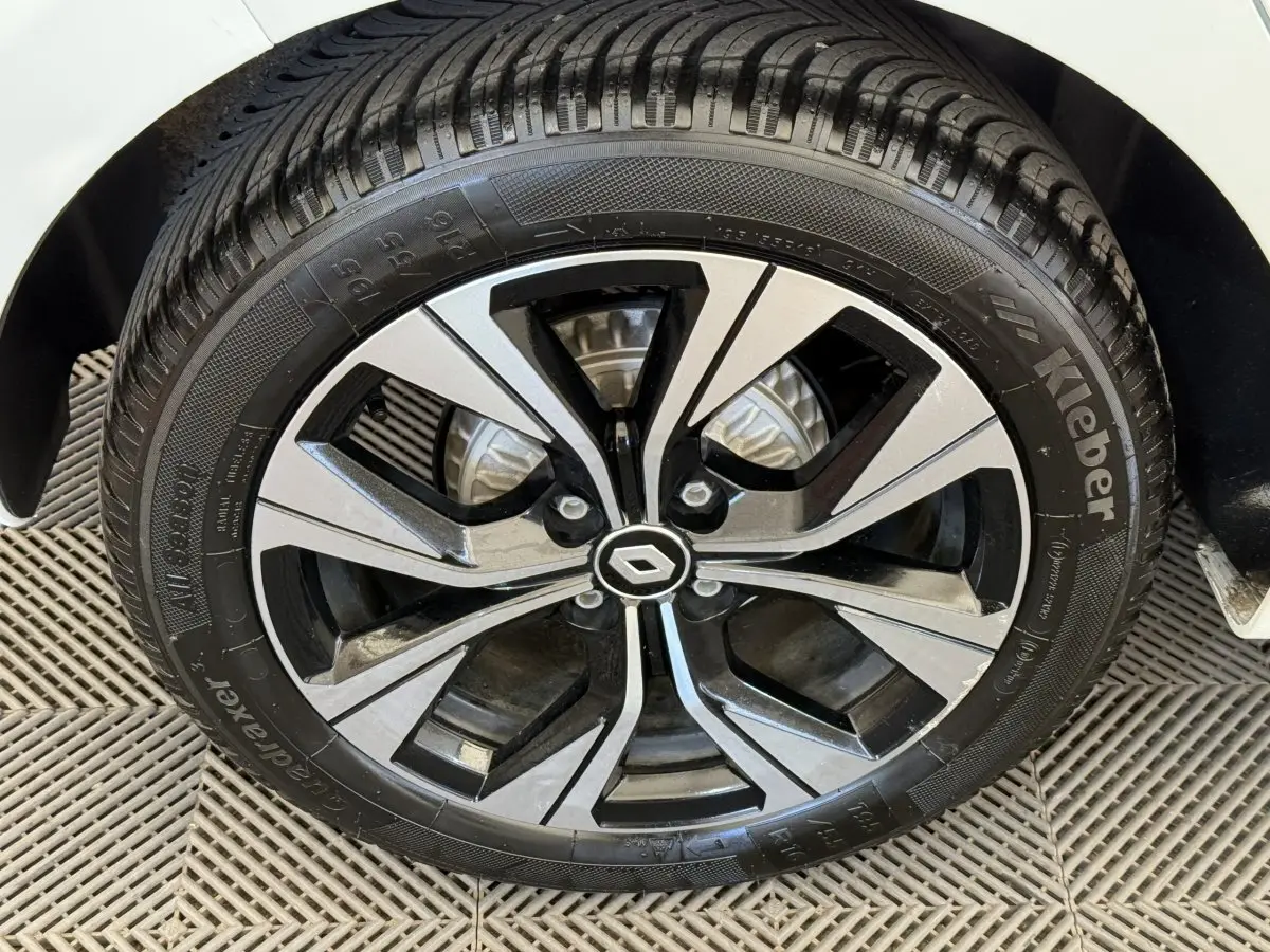 Gros plan sur la roue avant droite d'une Renault Clio blanche, mettant en valeur la jante alliage bicolore au logo central Renault.