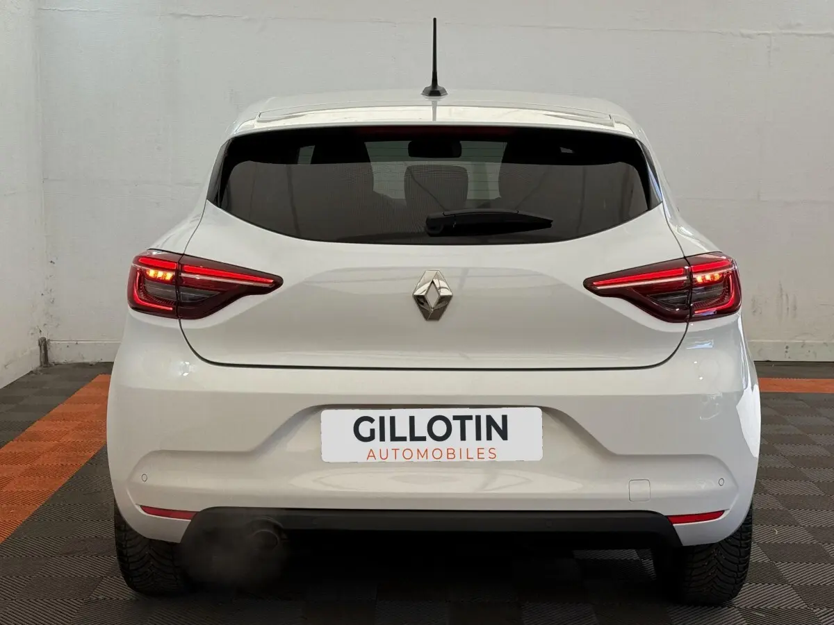 Vue arrière d'une Renault Clio blanche 2023 avec feux LED allumés et logo Renault centré sur le hayon.