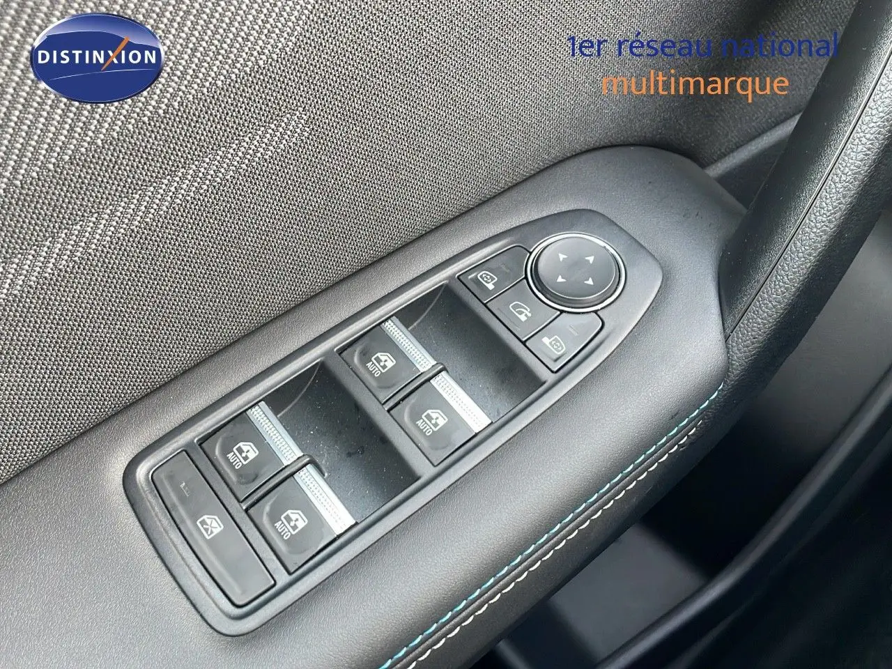 Gros plan sur les commandes des vitres et rétroviseurs côté conducteur du Renault Captur noir étoile métal avec surpiqûres bleues.