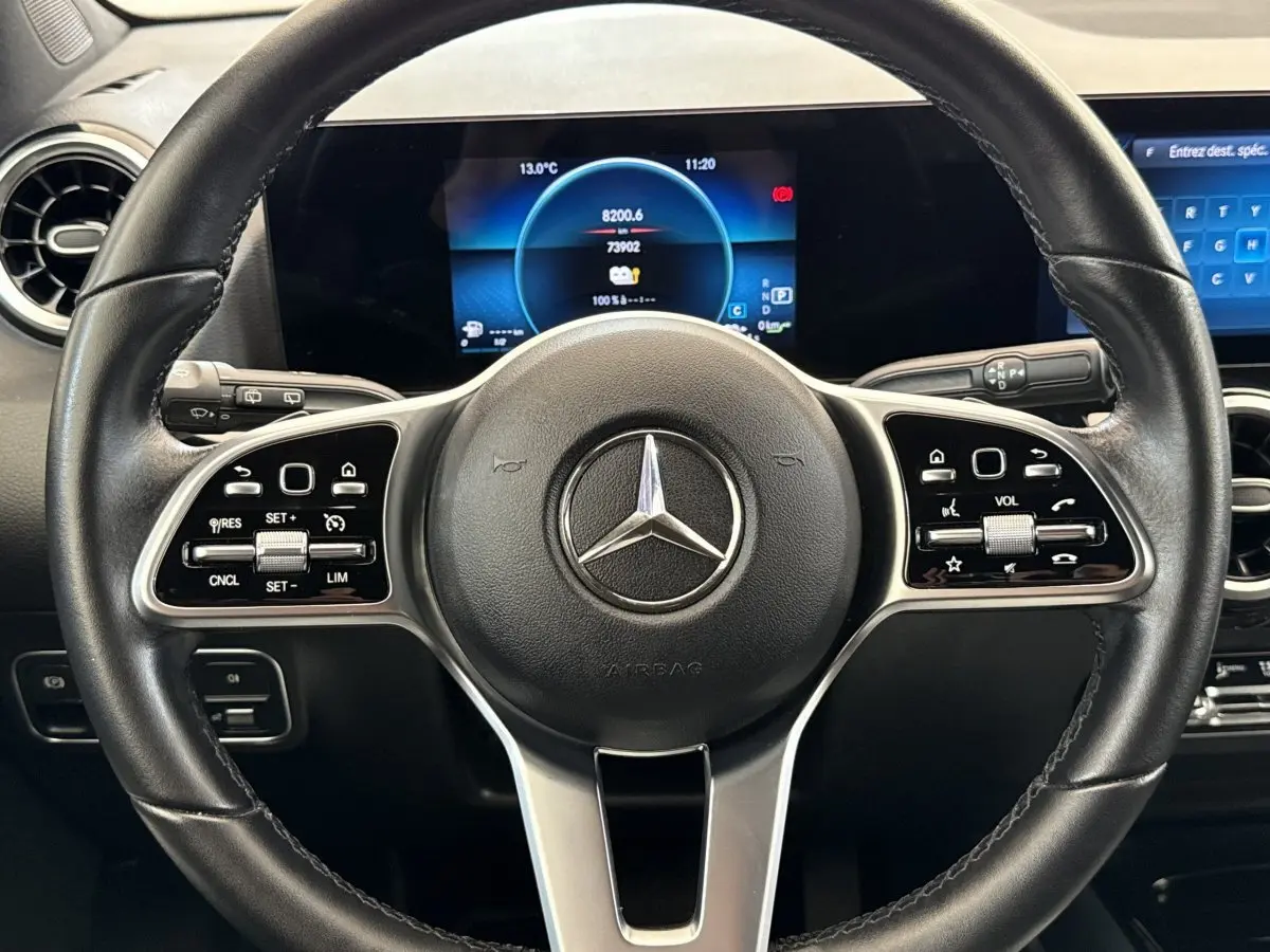 Vue intérieure centrée sur le volant cuir noir de la Mercedes GLA 250 e avec tableau de bord digital lumineux.