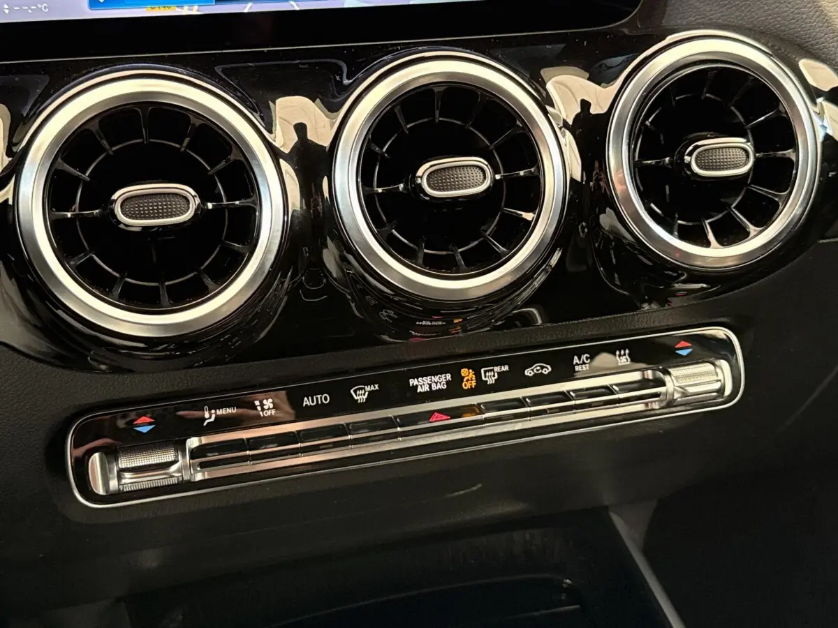 Détail du tableau de bord noir brillant du Mercedes GLA 250 e 2021 montrant trois aérateurs ronds chromés et commandes climatisation.