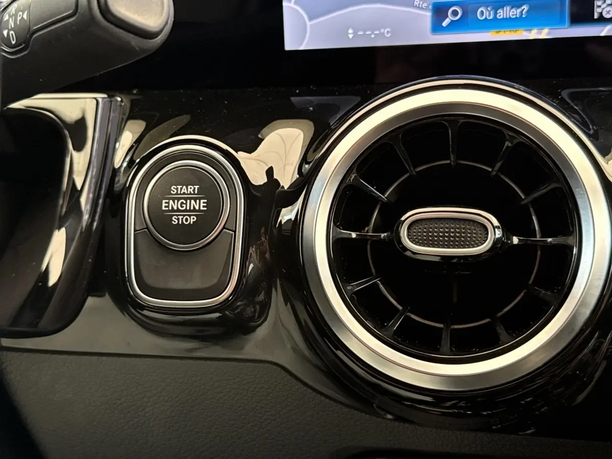 Détail intérieur montrant le bouton start/stop moteur et la sortie d’air circulaire chromée d’une Mercedes GLA 250 e bleu.