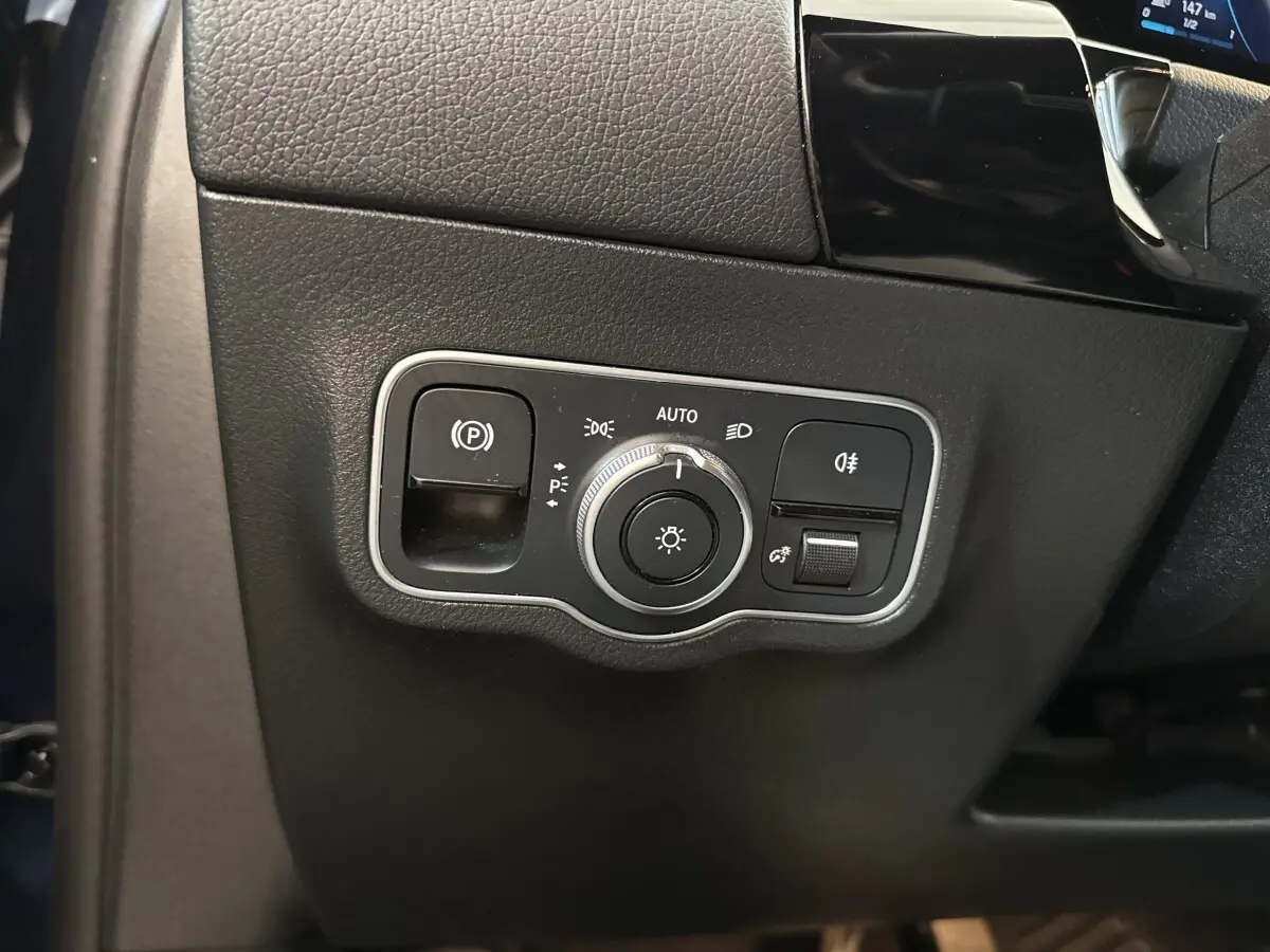 Gros plan sur le panneau de commande des phares et du frein à main électrique dans un Mercedes GLA 250 e bleu de 2021.
