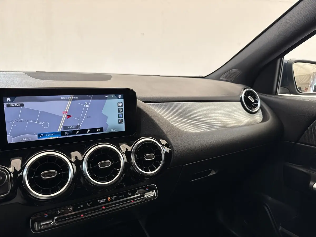 Vue intérieure côté passager du tableau de bord noir et argent avec écran tactile et aérateurs ronds chromés d’une Mercedes GLA 250 e bleu.