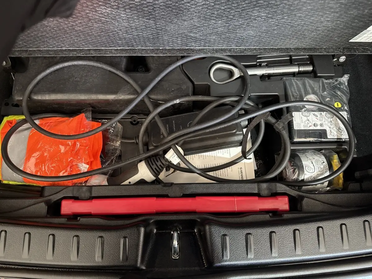 Coffre ouvert d’une Mercedes GLA 250 e bleu, montrant câble de recharge et équipement de sécurité rangés.