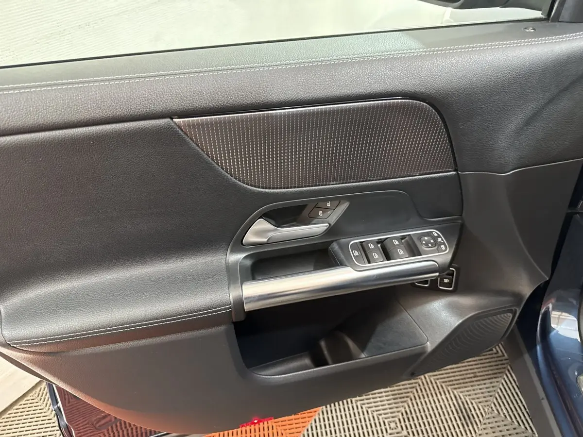 Vue intérieure côté gauche de la porte avant bleu du Mercedes GLA 250 e avec commandes fenêtres et poignée métal.