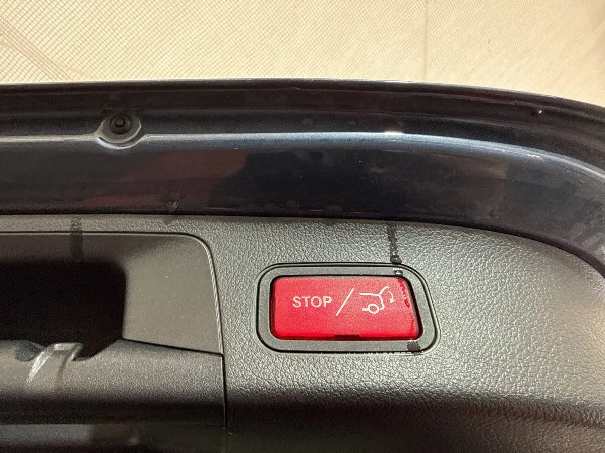 Gros plan sur le bouton rouge d'ouverture/fermeture électrique du coffre d'un Mercedes GLA bleu, vue intérieure du hayon.