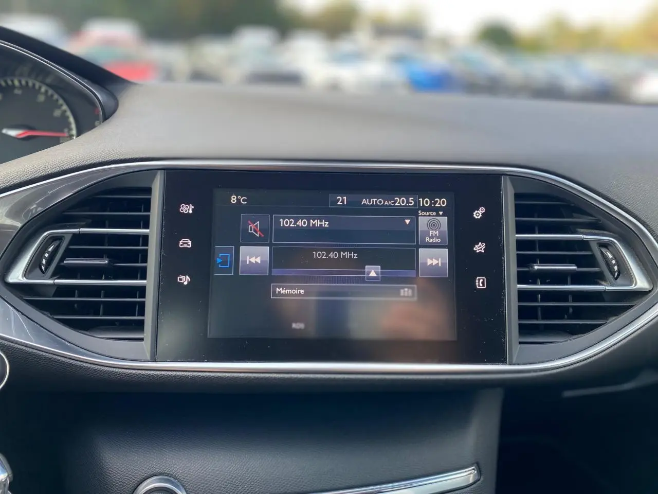 Écran tactile central de la Peugeot 308 2016 affichant la radio FM, entouré de grilles d'aération noires.