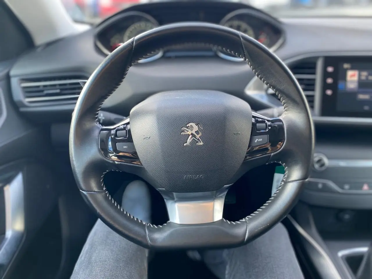 Volant cuir noir avec logo Peugeot au centre, vue frontale de l'habitacle de la 308 gris aluminium de 2016.