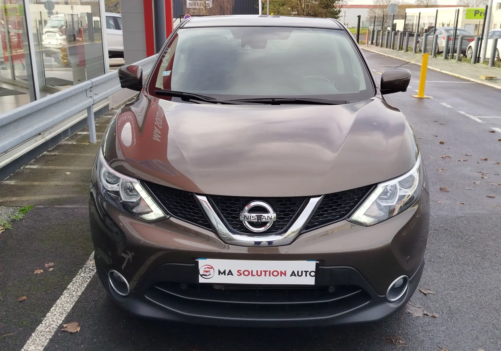 Vue avant d'un Nissan Qashqai bronze Ultime 2017 avec calandre chromée et phares allumés en extérieur.