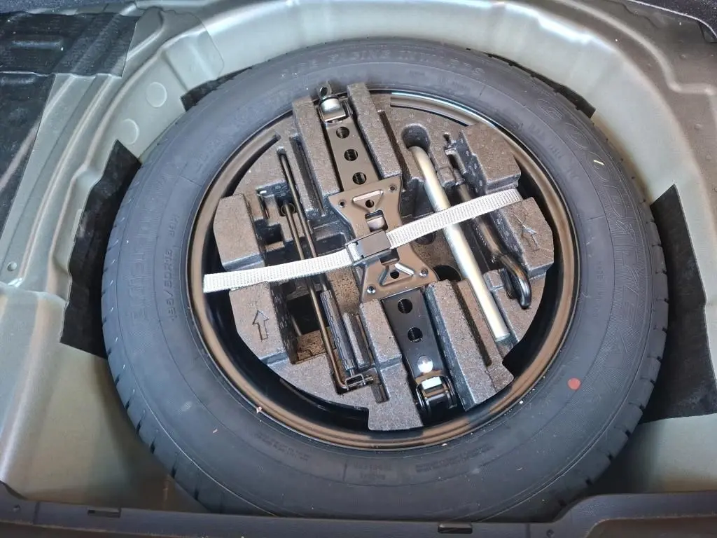 Vue de dessus de la roue de secours et des outils de bord rangés dans le coffre d’un Skoda Kamiq gris foncé 2023.