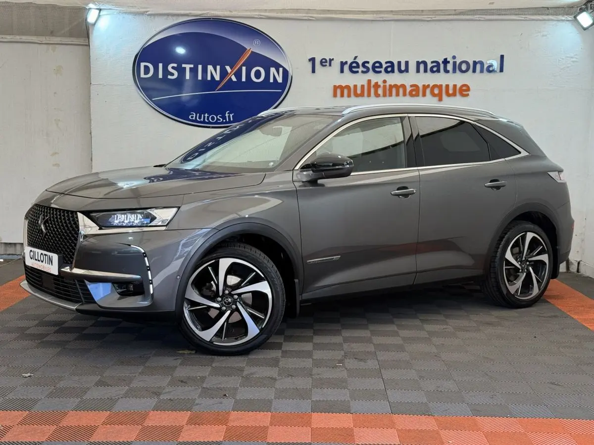 Vue de profil côté gauche d'un DS7 Crossback gris foncé avec jantes alliage et toit chromé dans un showroom.
