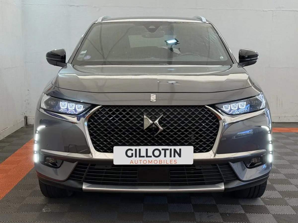 Vue frontale d’un DS7 Crossback gris foncé avec calandre noire, feux LED allumés et signature lumineuse verticale.