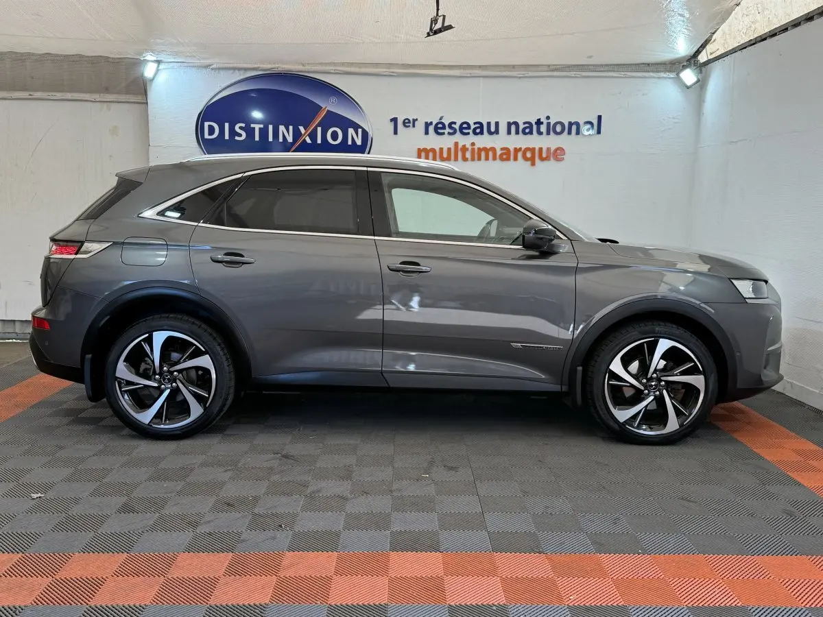 Vue latérale droite d'un DS7 Crossback gris foncé avec jantes alliage bicolores et vitres teintées dans un showroom.