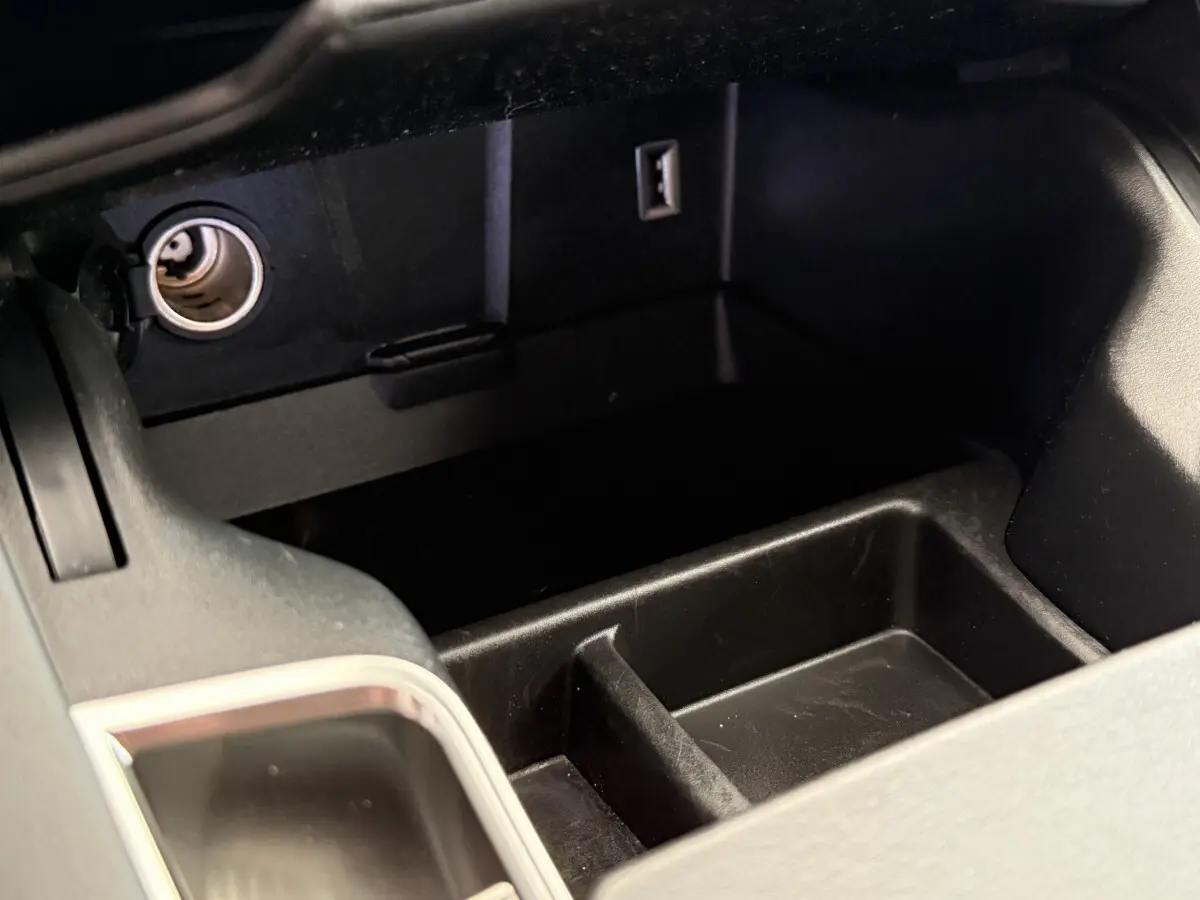 Vue rapprochée du rangement central noir avec prise 12V et port USB dans le DS7 Crossback gris foncé.