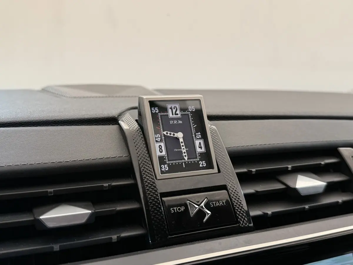 Gros plan sur l'horloge analogique centrale et les aérateurs du tableau de bord du DS7 Crossback gris foncé.
