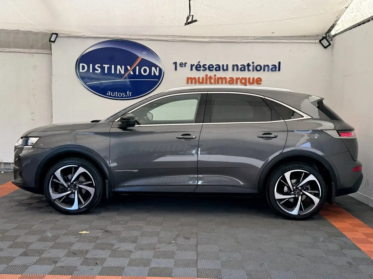 Vue latérale droite d'un DS7 Crossback gris foncé avec jantes alliage bicolores et toit chromé dans un showroom.