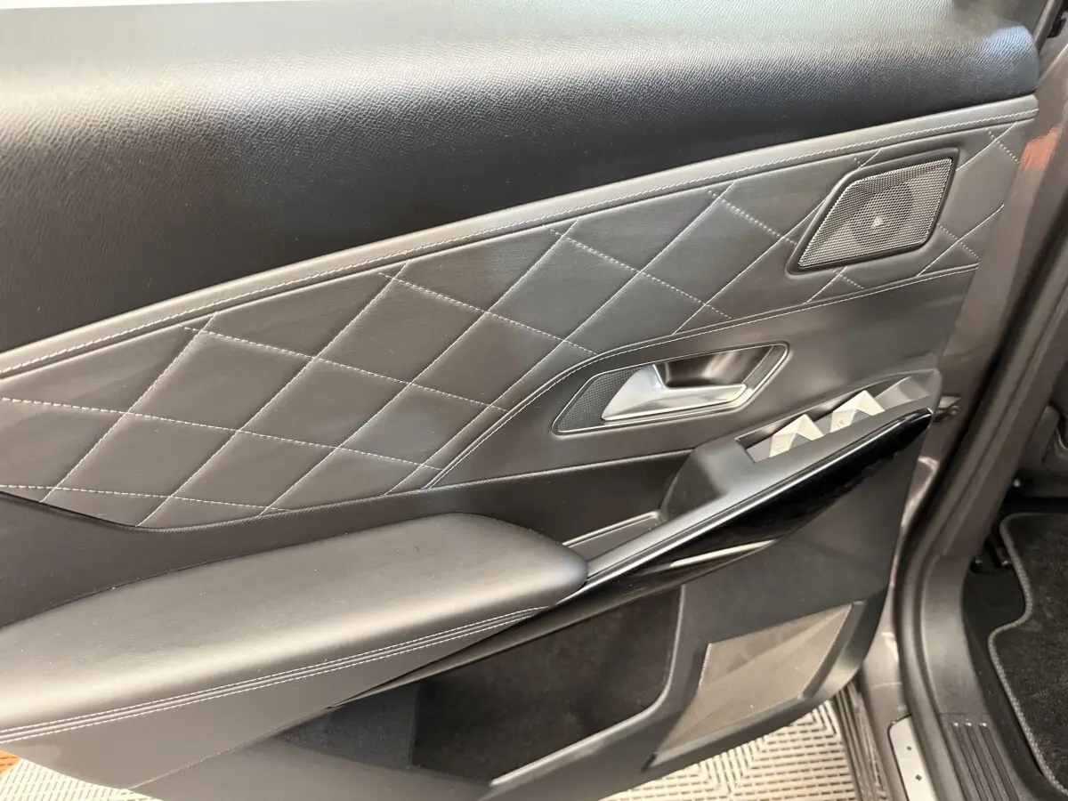 Gros plan sur la garniture intérieure côté gauche de porte en cuir noir matelassé avec commandes vitres et haut-parleur intégré.