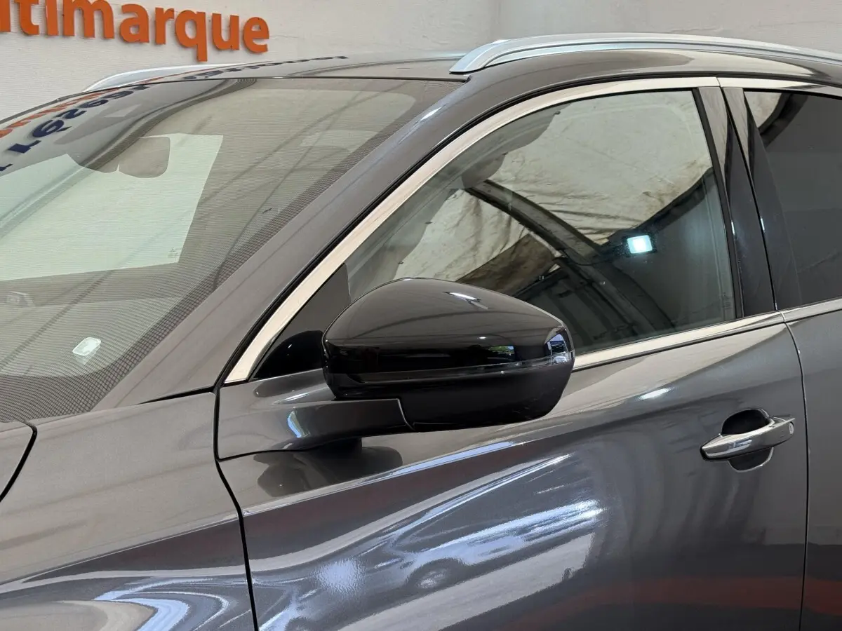 Vue côté gauche rapprochée du DS7 Crossback gris foncé, mettant en valeur la vitre teintée et le rétroviseur noir brillant.