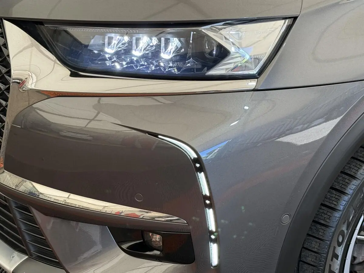 Gros plan sur l’avant droit gris foncé du DS7 Crossback avec phares LED et feux diurnes verticaux allumés.