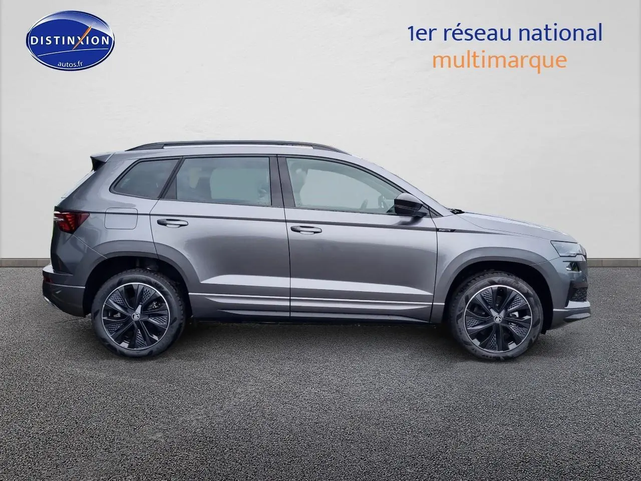 Profil côté gauche du Skoda Karoq gris graphite 2025 avec jantes alu sport et barres de toit visibles.