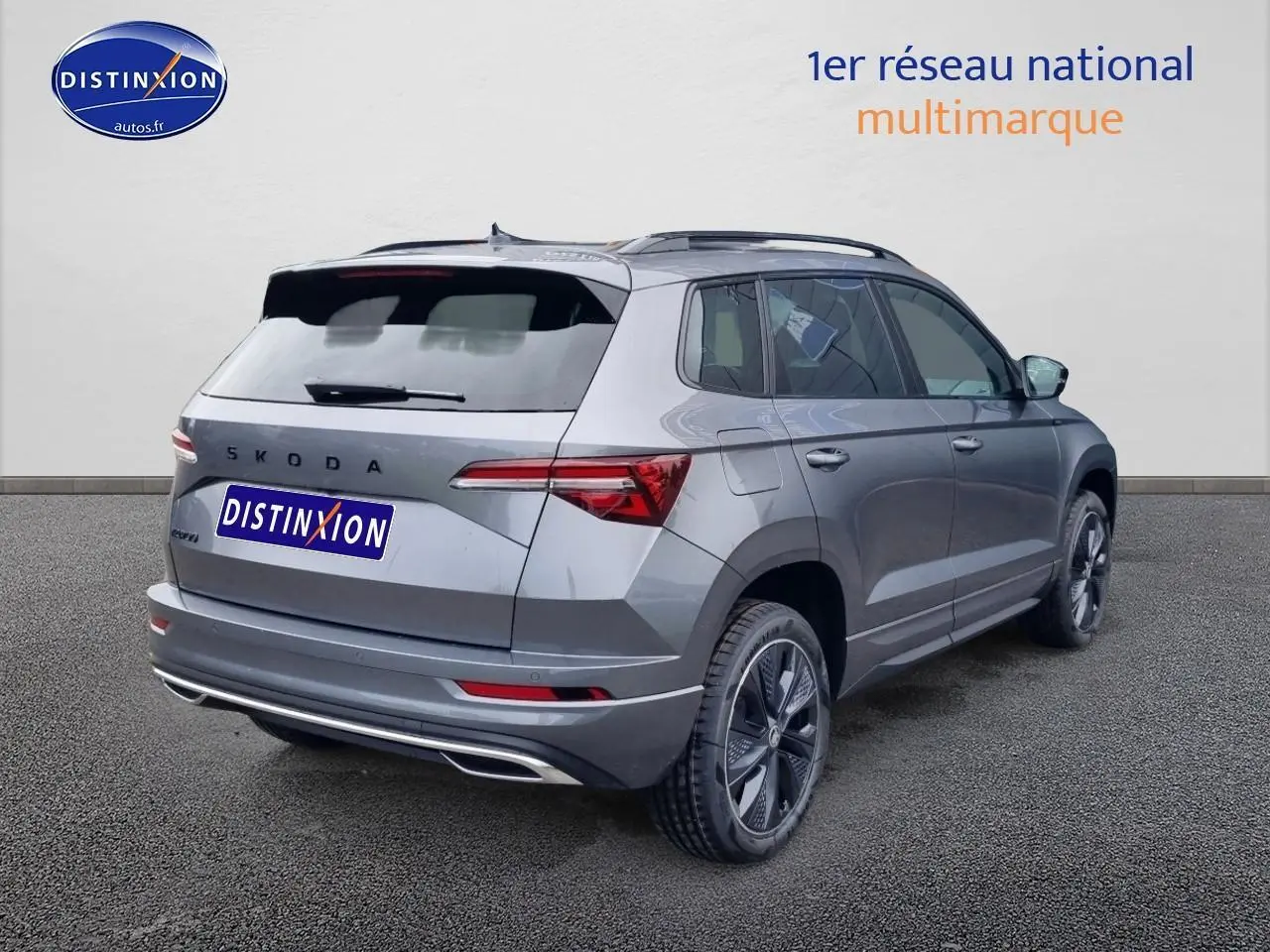 Vue 3/4 arrière droite d'un Skoda Karoq gris graphite 2025 avec jantes alu et barres de toit visibles.