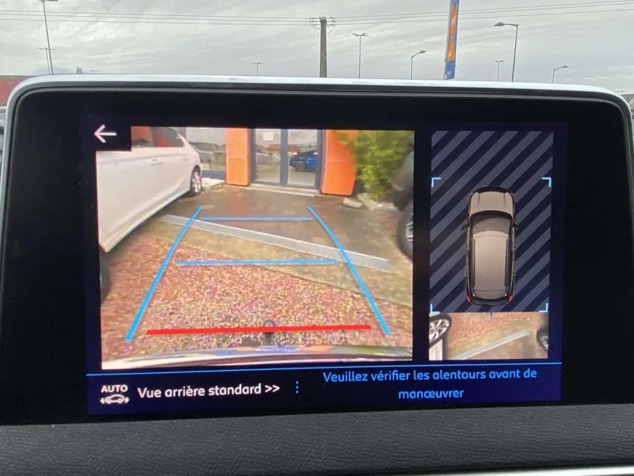 Écran tactile du Peugeot 3008 montrant la caméra de recul avec vue arrière et vue de dessus du véhicule marron foncé.