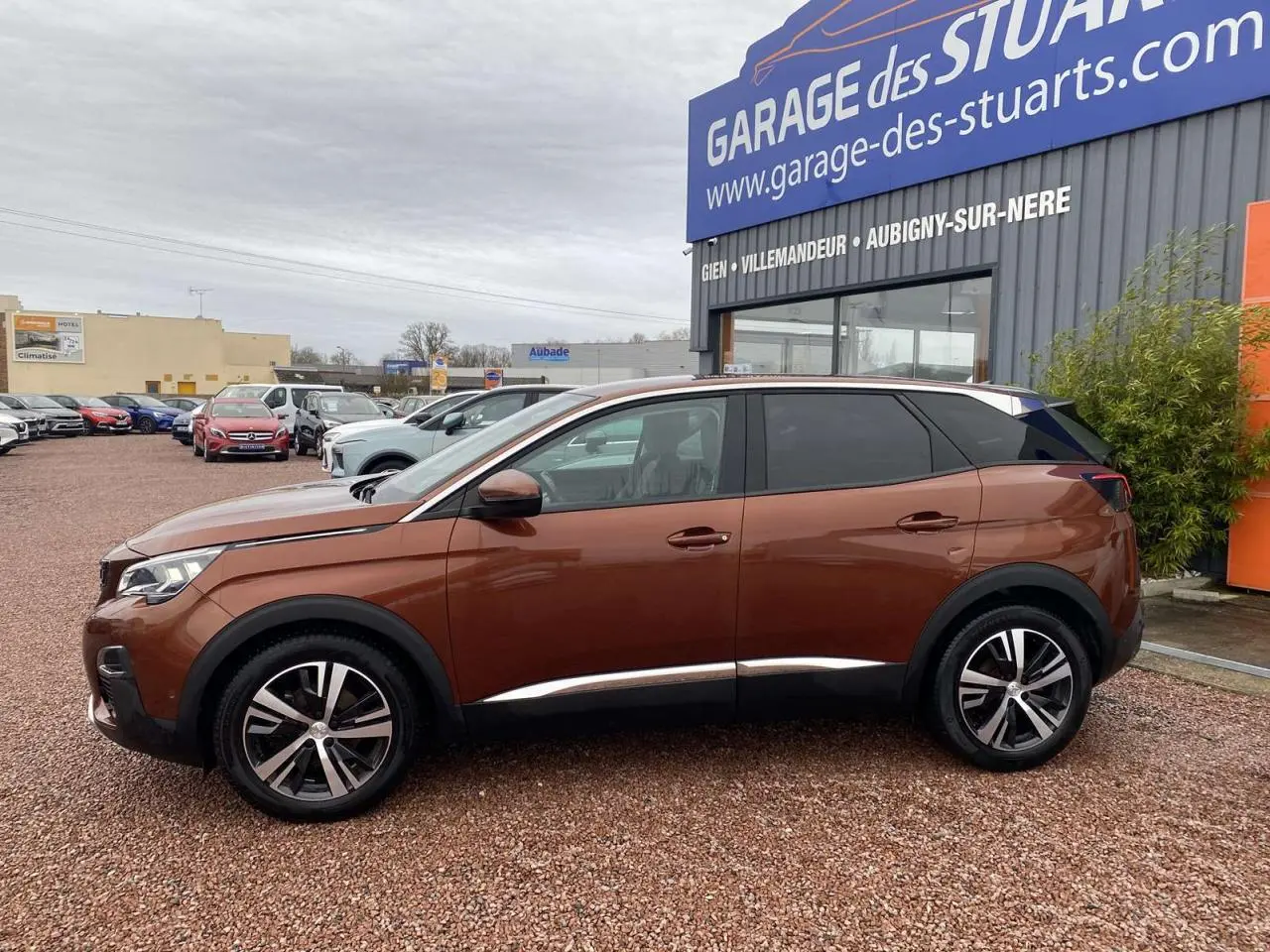 Profil côté gauche du Peugeot 3008 marron foncé avec jantes alliage 18 pouces, stationné devant un garage.
