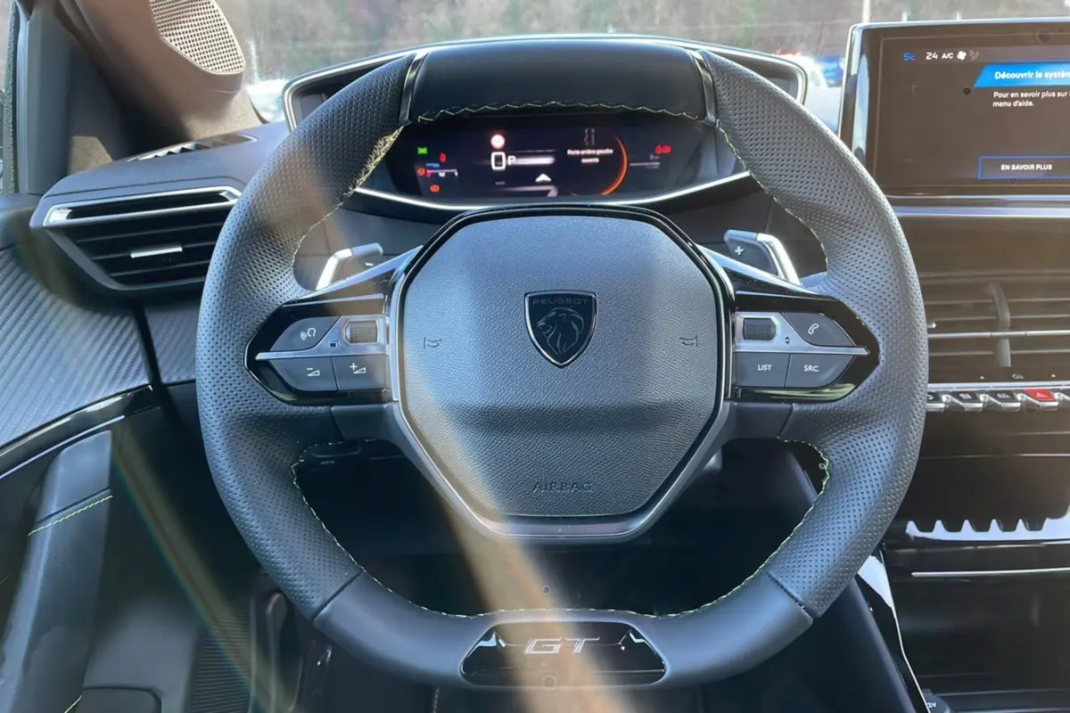 Volant multifonction noir avec logo Peugeot et badge GT, tableau de bord digital et écran central d'une 208 Hybrid 136 GT Plus 2024.