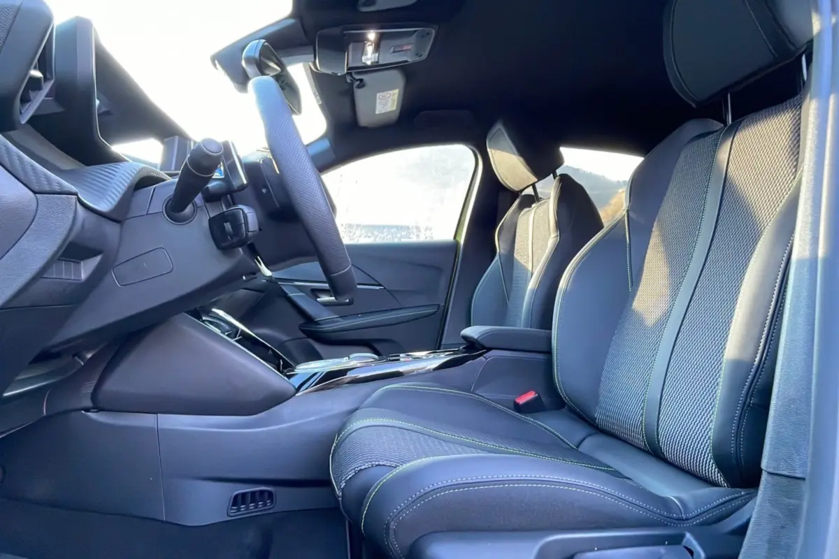 Intérieur avant droit de la Peugeot 208 HYBRID 136 GT PLUS 2024 avec sièges en cuir noir et surpiqûres vertes