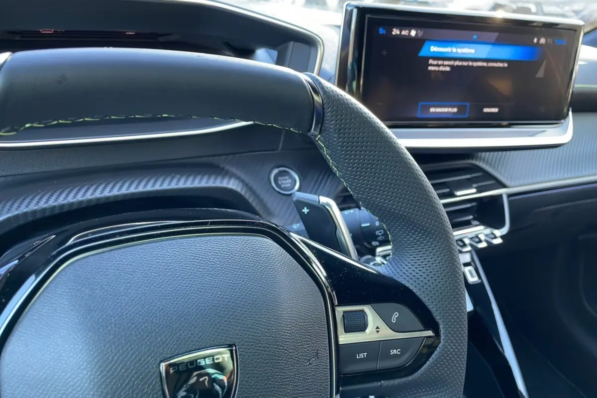Intérieur de la Peugeot 208 Hybrid 136 GT Plus 2024, vue sur le volant perforé et l'écran tactile central.