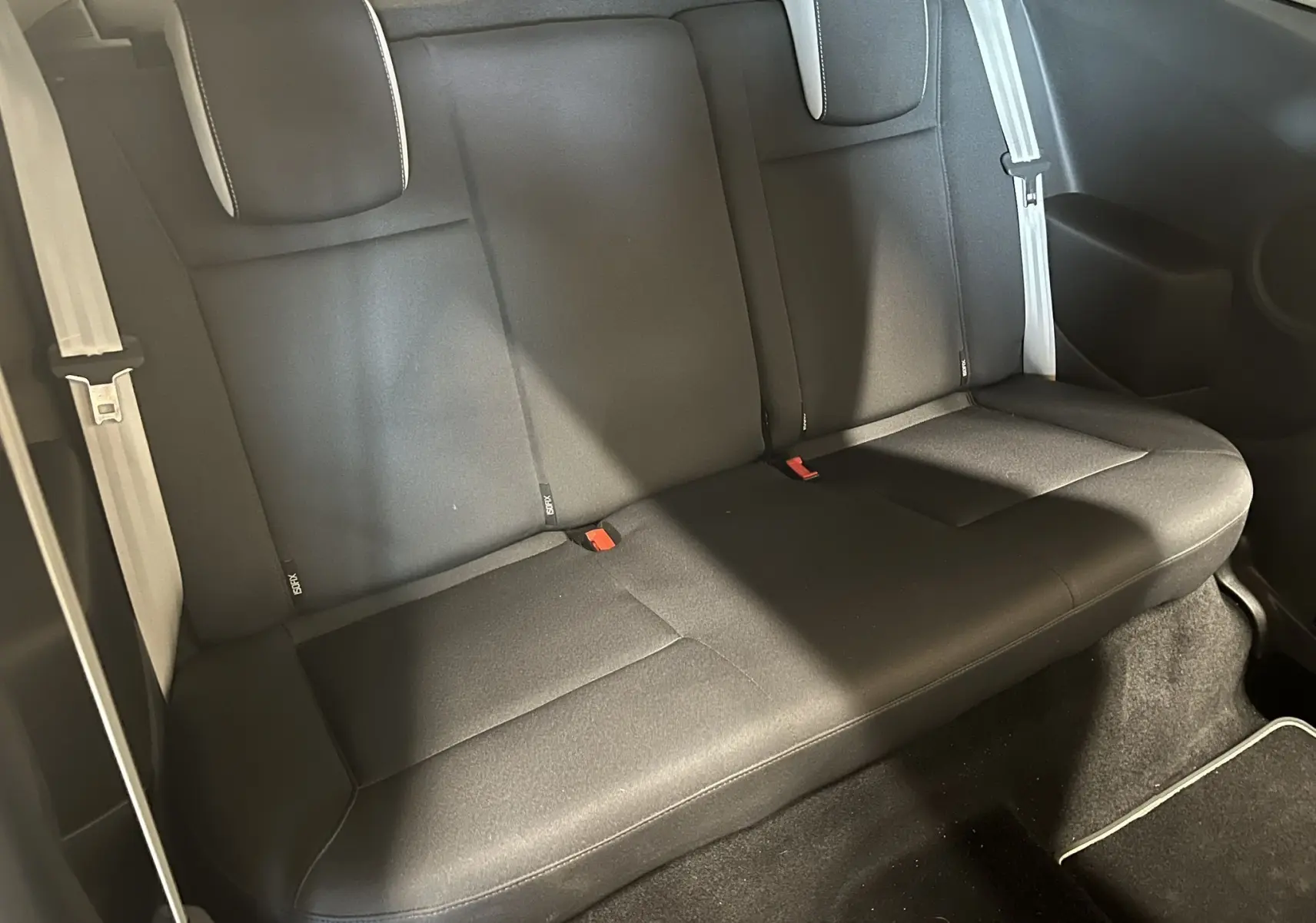 Vue intérieure arrière de la banquette noire de la Renault Clio III RS 20th Anniversary avec ceintures grises et fixations Isofix visibles.