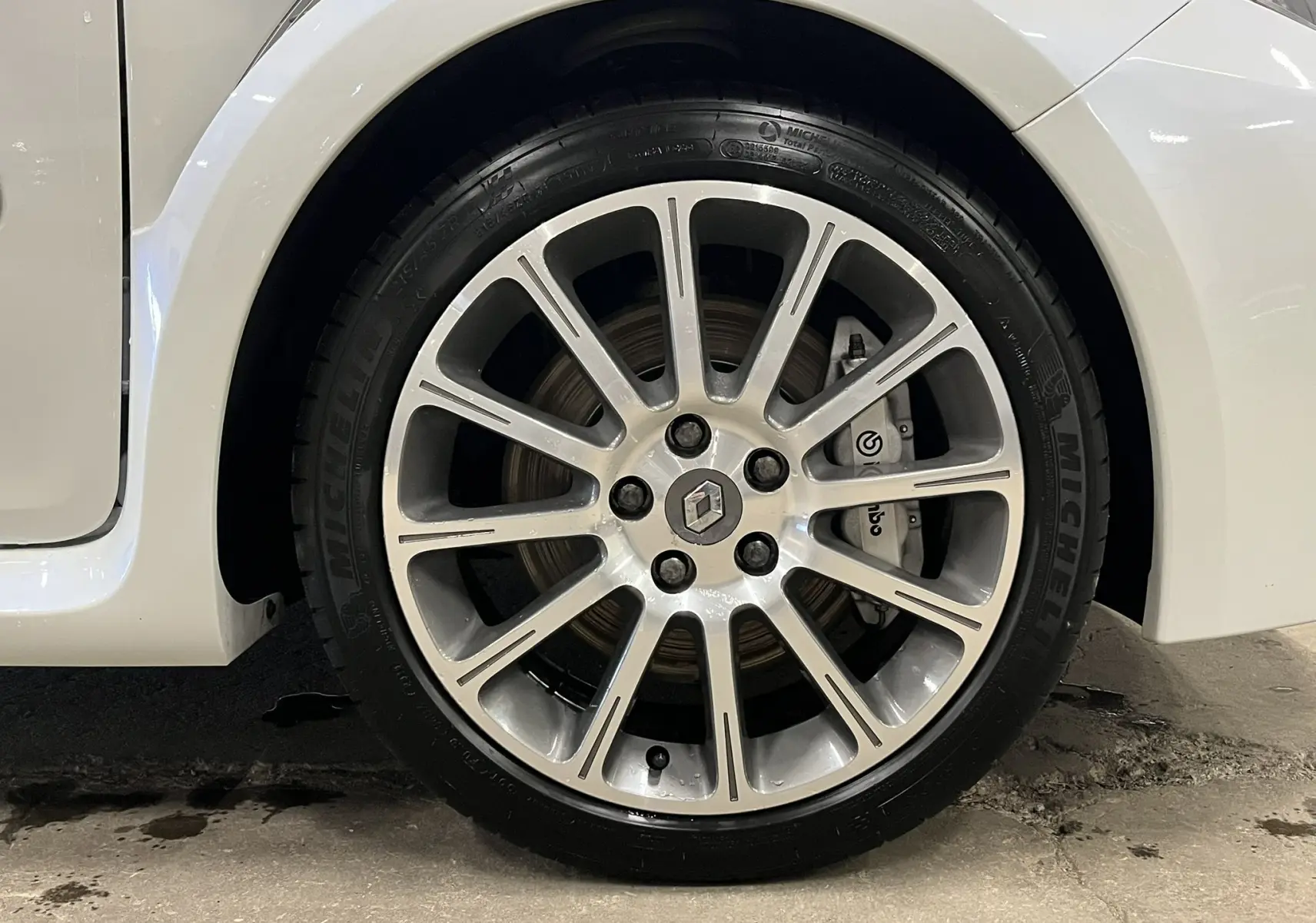 Gros plan sur la roue avant gauche de la Renault Clio III RS 20th Anniversary blanc nacré avec jante alliage et étrier Brembo visible.