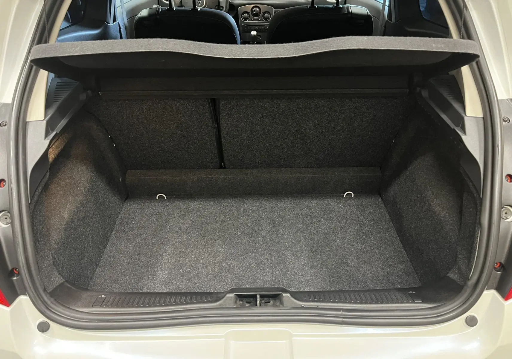 Coffre ouvert vu de l'arrière d'une Renault Clio III RS 20th Anniversary blanc nacré avec intérieur noir.