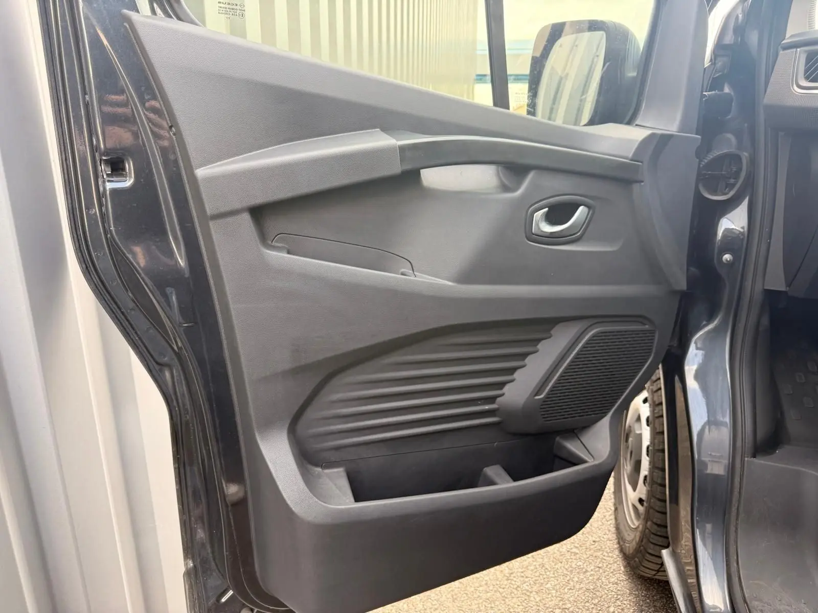 Vue rapprochée de la porte latérale gauche ouverte du Renault Trafic gris comète, montrant les rangements et la poignée intérieure.