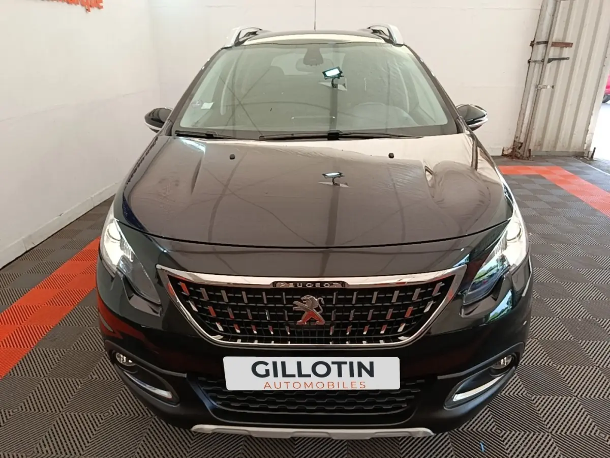 Peugeot 2008 noir vue de face dans un garage, avec calandre chromée et feux LED allumés.