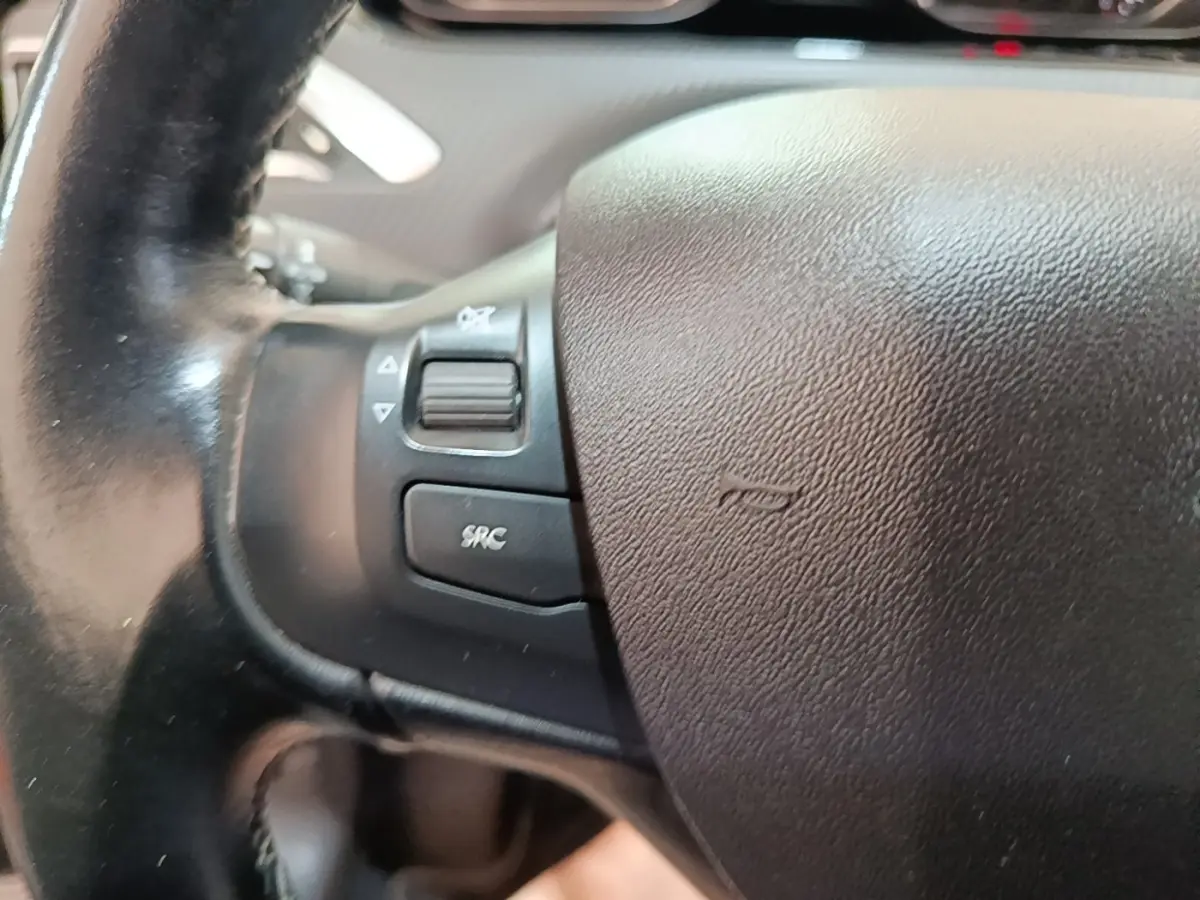 Gros plan sur le volant noir de la Peugeot 2008 Puretech 130, avec commandes audio intégrées à gauche.