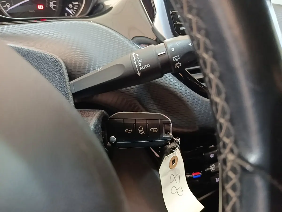 Gros plan sur le volant cuir et la clé noire du Peugeot 2008 Puretech 130, avec commandes de vitres et tableau de bord partiel.
