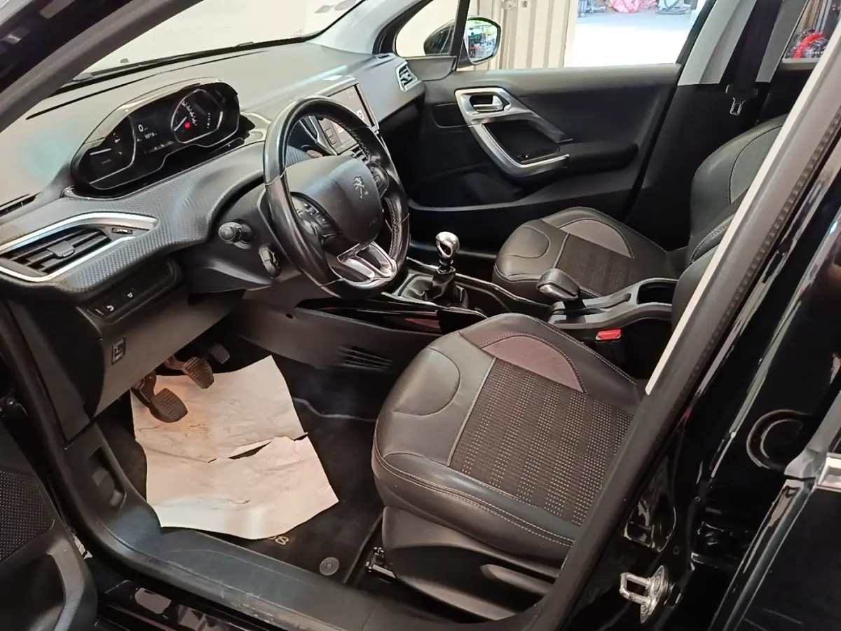 Vue intérieure côté conducteur de la Peugeot 2008 noire, montrant le volant cuir, tableau de bord et sièges avant en tissu.